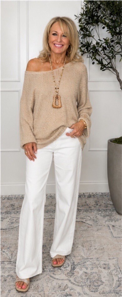 Donna in a beige off-shoulder sweater and white trousers